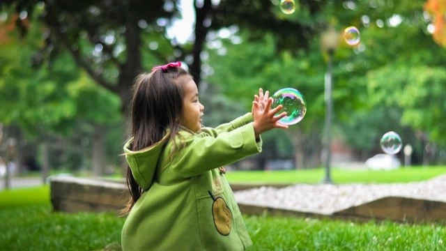 Toddler playing with bubbles outdoors, enjoying cognitive activities for infants that stimulate sensory exploration and hand-eye coordination.