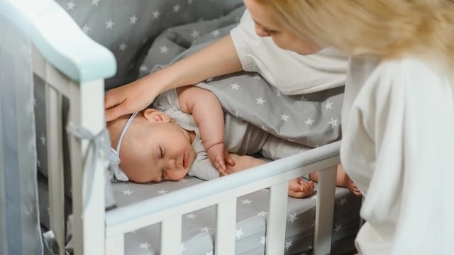 Mother gently comforting her newborn baby sleeping in a bassinet with star-patterned bedding, showcasing a nurturing and safe sleep environment for infants.