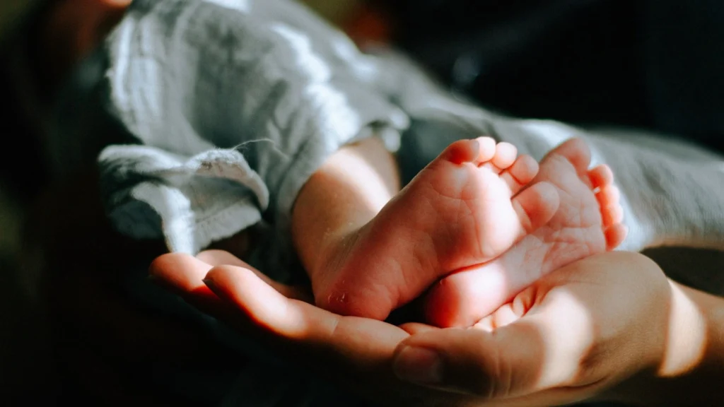 Close-up of a newborn's feet resting gently on a parent's hand, illustrating the lap hold position as a safe and comforting way to hold a newborn.