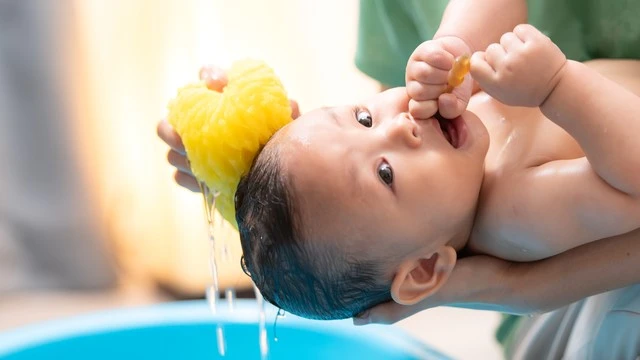 A caregiver gently using a sponge to rinse a newborn's head during a sponge bath, showcasing proper technique for how to sponge bath a newborn.