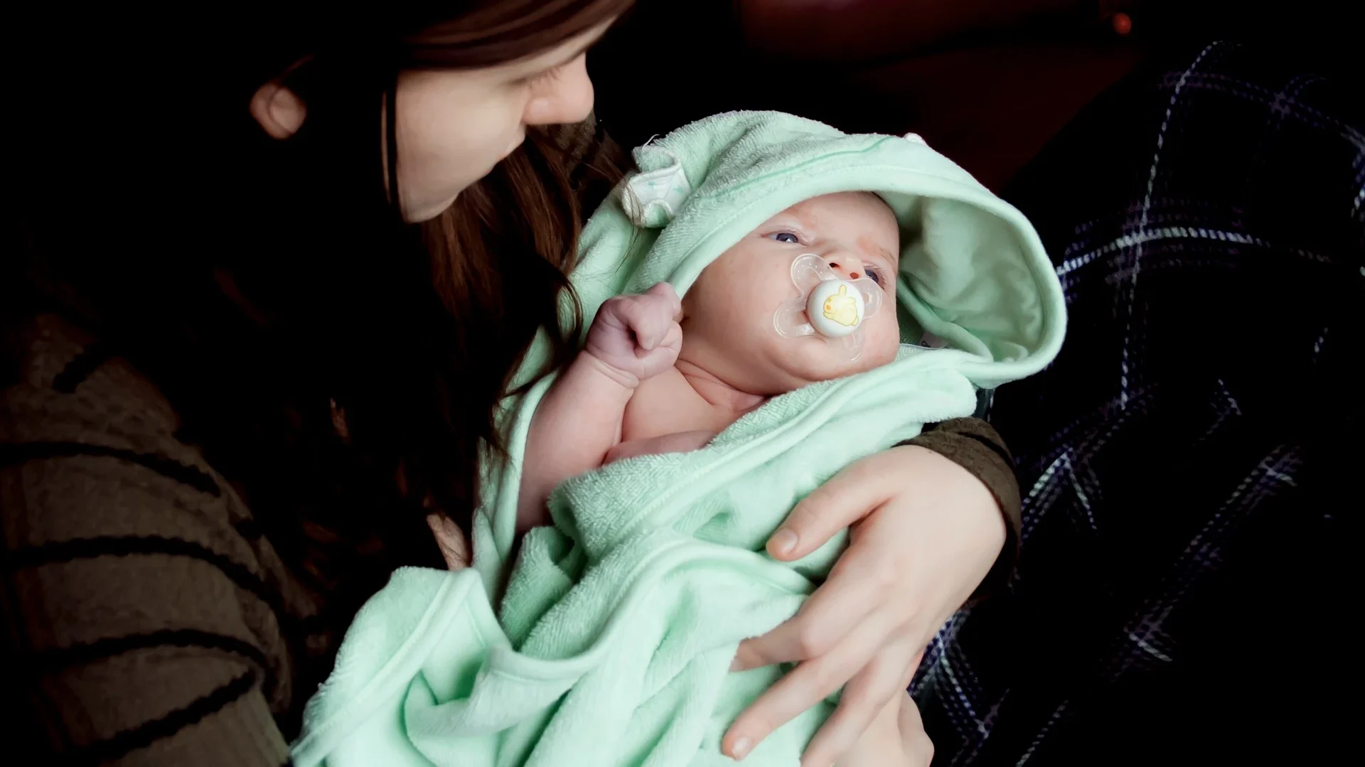 A mother holding a newborn wrapped in a soft green towel after a sponge bath, demonstrating the final steps of how to sponge bath a newborn