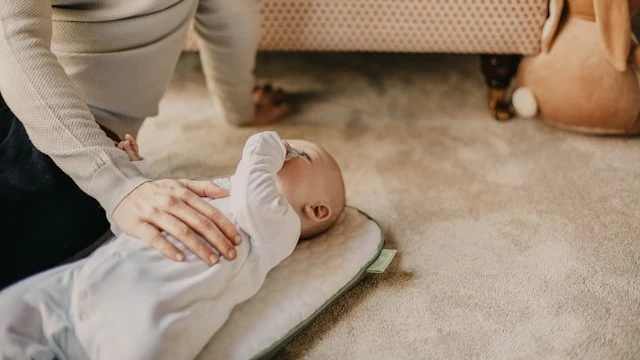 Caregiver comforting a newborn lying on a soft mat, emphasizing the importance of identifying signs of poor feeding in newborns for their well-being.