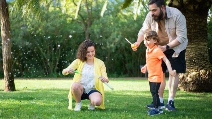 A happy family playing with bubbles in a park, creating joyful memories together. Learn practical ways to have patience with a toddler.