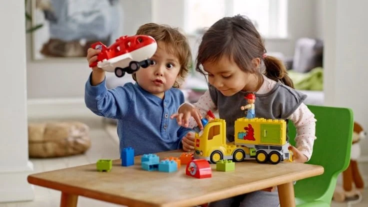 Two young children playing with toy vehicles and blocks, engaging in social skills development by practicing sharing and cooperative play.