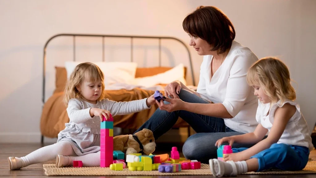 Mother helping toddlers build with colorful blocks as part of fine motor skills activities for toddlers.