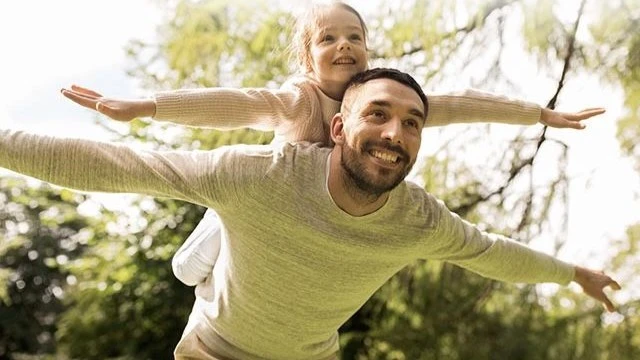 Father demonstrating parenting strengths by playing airplane with his smiling daughter outdoors, symbolizing emotional connection and balance in parenting strengths and weaknesses.