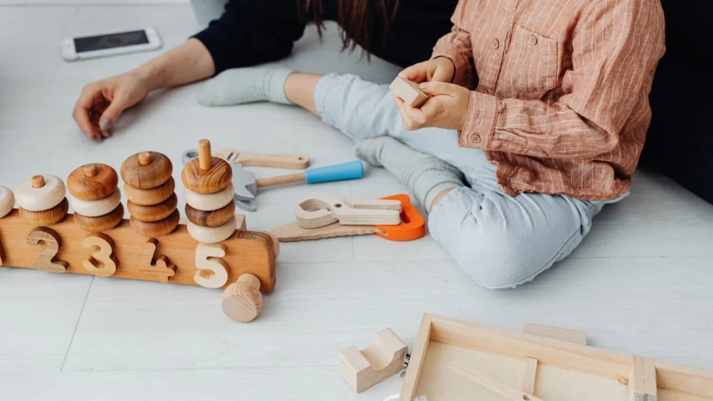 Toddler practicing fine motor skills with wooden stacking toys and blocks, part of fine motor skills activities for toddlers.