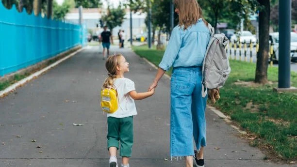 A mother walking hand-in-hand with her child wearing a backpack on the way to school.