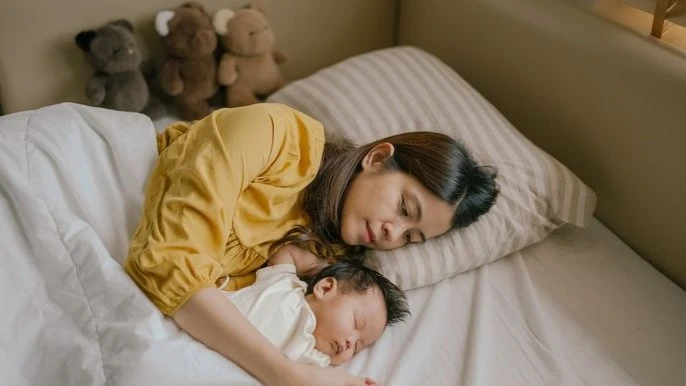 Mother resting peacefully with her newborn in bed, symbolizing emotional bonding and mental health tips for parents through restful moments.